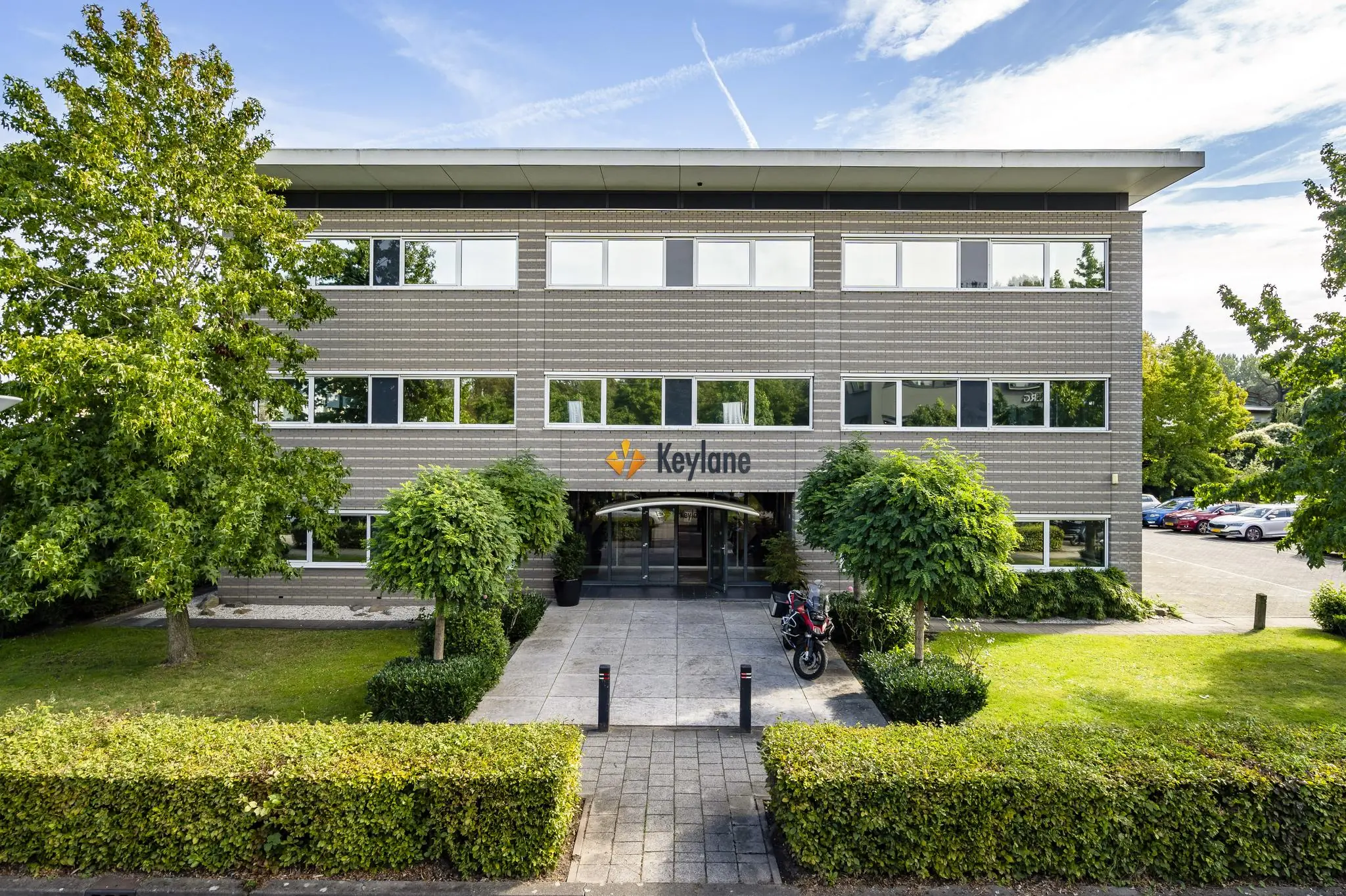 Vooraanzicht van het kantoorgebouw van Keylane aan de Jan Leentvaarlaan, omgeven door groen en parkeerplaatsen.